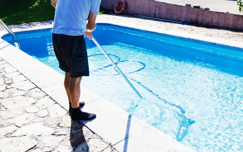 Man cleaning the pool at home, standing with the cleaner device, doing chores